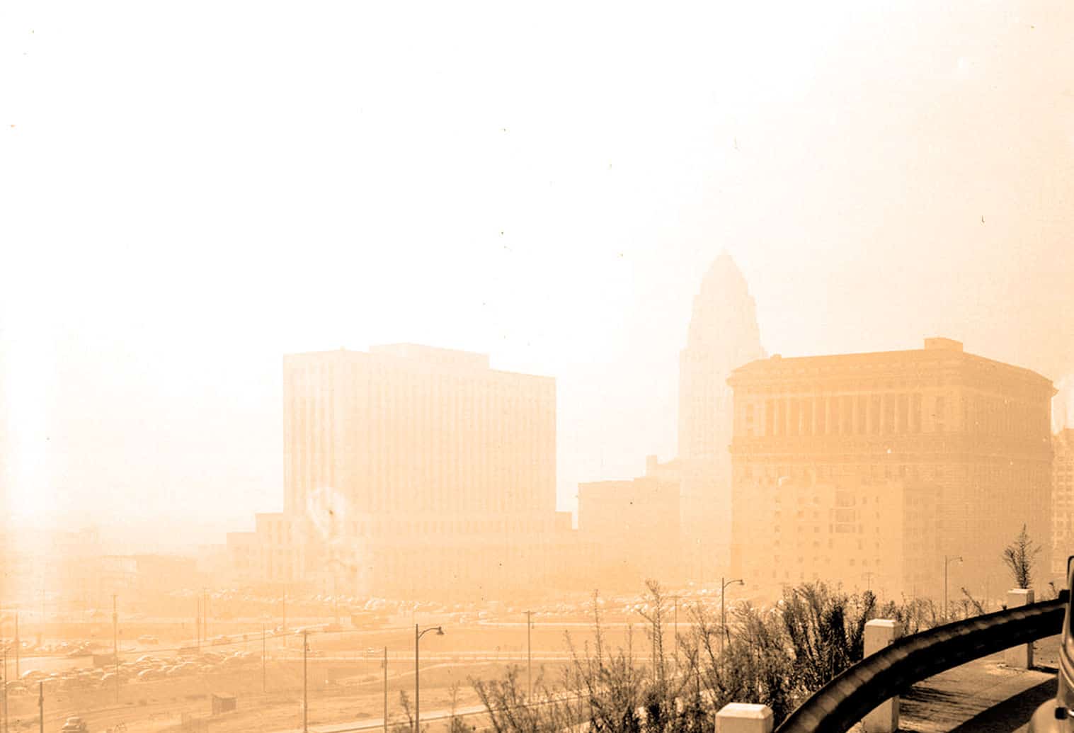 Dusty city skyline enveloped in haze, featuring historic buildings and a parking lot, evoking a nostalgic atmosphere for audio news, history, and music archives.
