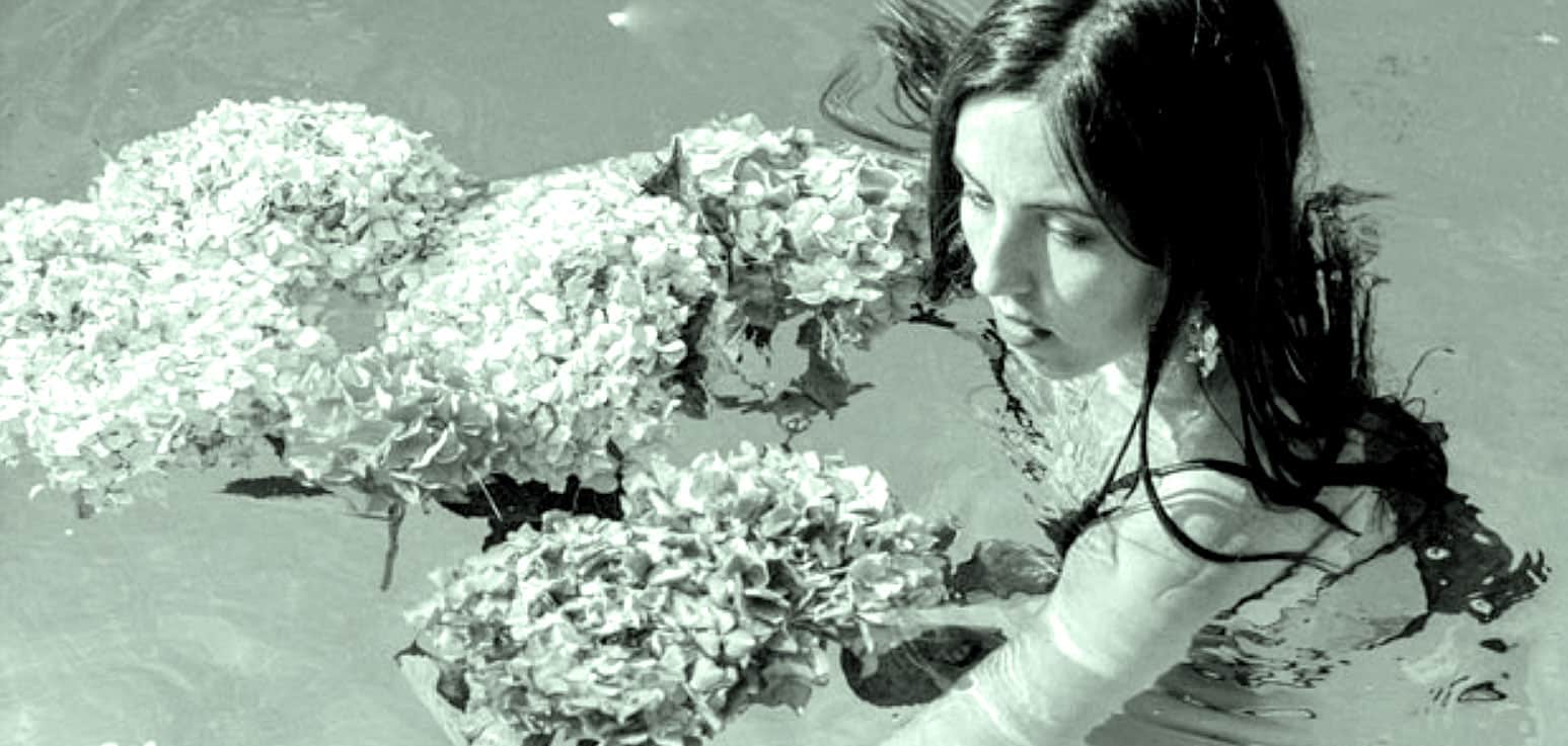 A woman with long dark hair in a swimsuit holding white hydrangea flowers in a pool, showcasing relaxation and nature, perfect for music, history, news, and sound archive themes.