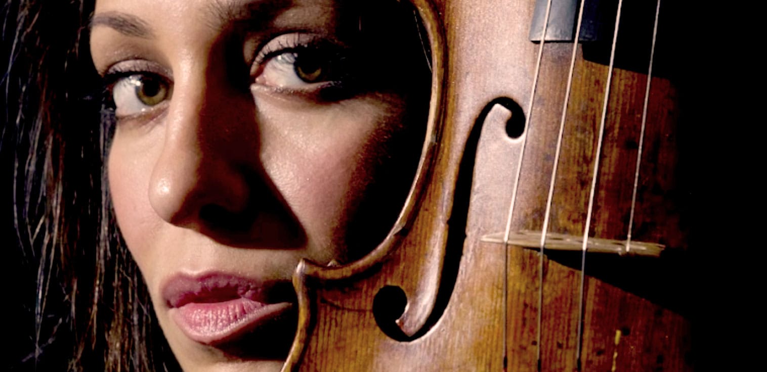 Close-up of a woman with piercing eyes holding a wooden violin, emphasizing her intense expression and the instrument’s details, highlighting music, history, and sound archive themes.
