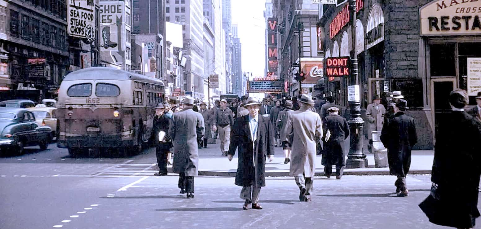 A busy city street scene from the 1940s showing pedestrians in vintage suits and hats crossing the road, with classic cars and an old trolley, featuring neon signs and storefronts in a bustling downtown area.