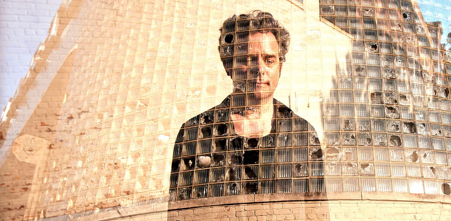 A mural featuring a man with dark curly hair, painted on a building made of glass blocks, blending art with architecture, representing creative expression and urban culture.
