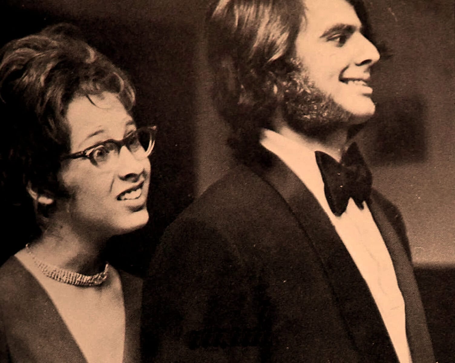 Vintage black and white photo of a woman and a man dressed in formal attire, showcasing classic 1960s fashion and style, highlighting historical and cultural music icons.
