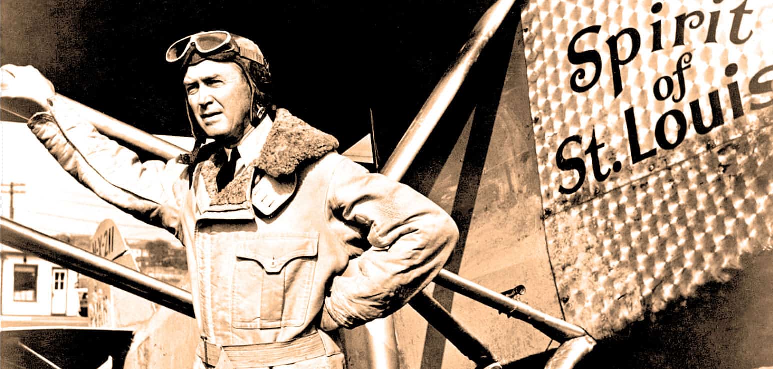 Vintage pilot standing beside airplane with "Spirit of St. Louis" sign, representing historical aviation milestones and iconic travel moments, ideal for news archives and history enthusiasts.