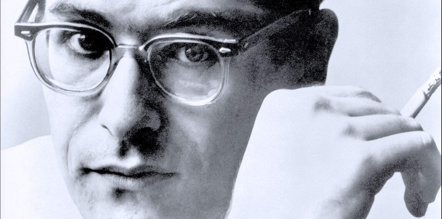 Close-up black and white portrait of a man wearing glasses, holding a cigarette, representing audio archives, historical news, and music collections from Past Daily.
