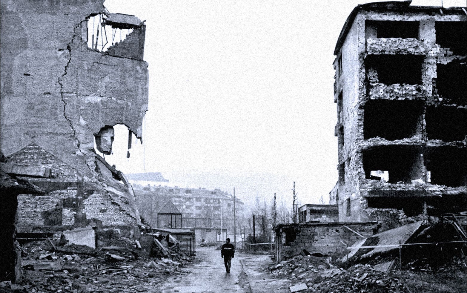 Destroyed buildings with extensive damage and a lone person walking through a war-torn area, representing historical conflict, destruction, and resilience, captured in black and white for dramatic effect.