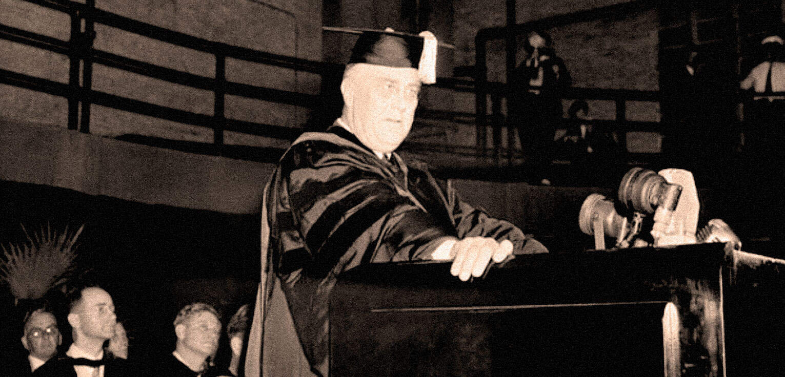 Historic photograph of a university graduation ceremony, featuring a graduate in cap and gown preparing to receive their diploma. The scene highlights academic achievement captured in vintage black and white.