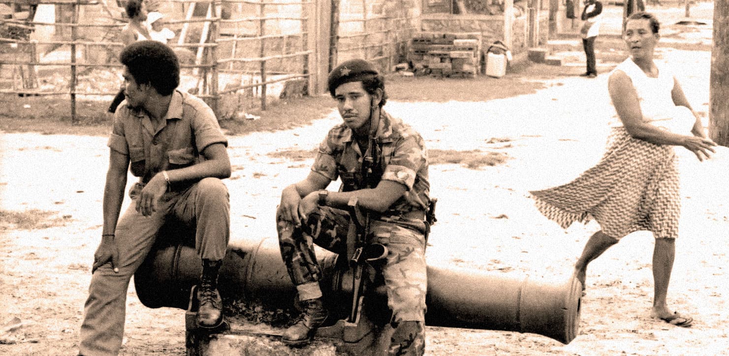 Old black and white photo of young soldiers sitting on a large artillery shell in a rural village scene, with a woman walking nearby, historical military and community life, vintage wartime image.