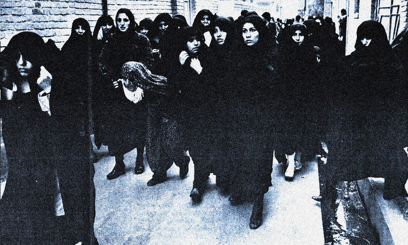 Women protesting against violence and oppression, wearing black clothing and veils in an urban street setting.