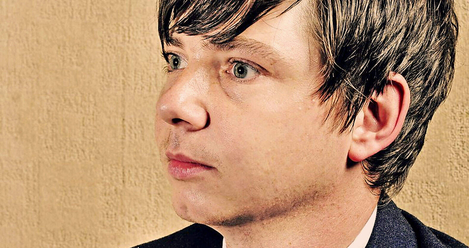 Close-up portrait of a young man with dark hair, blue eyes, and fair skin, emphasizing his thoughtful expression, suitable for images representing history, music, and news archives.