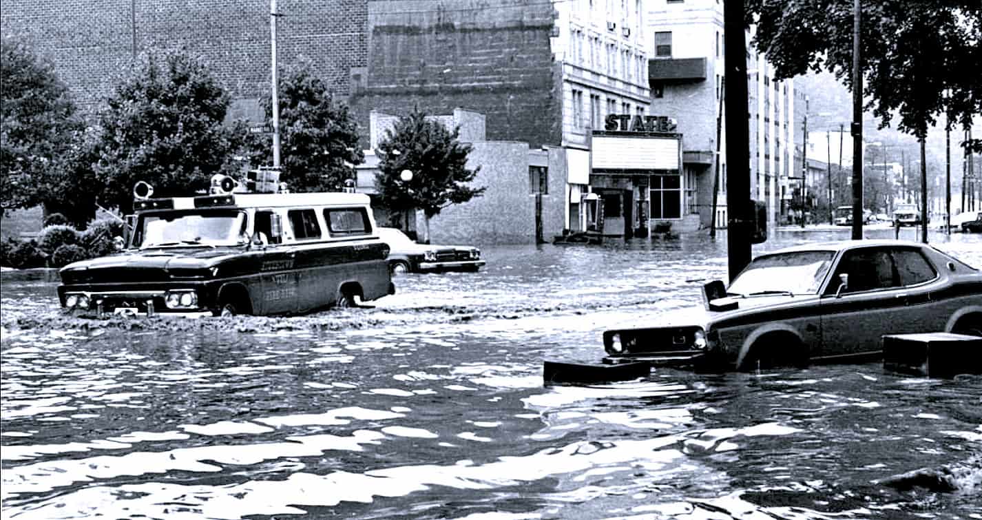 Flooded city street with submerged cars during heavy rain, historical urban water damage scene, archival weather event image for news and history archives.