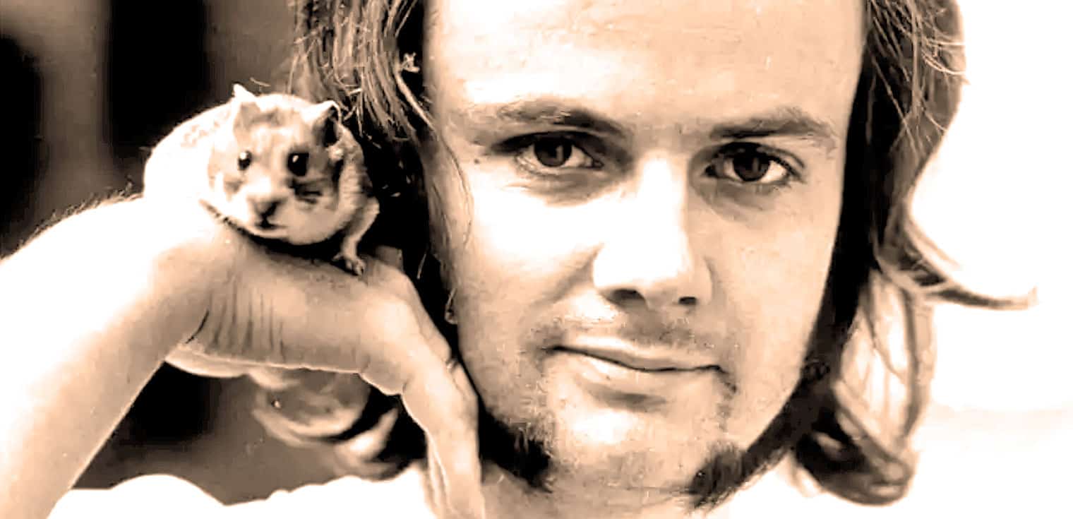 A man with long hair holding a small hamster on his shoulder, capturing a moment of companionship and curiosity.