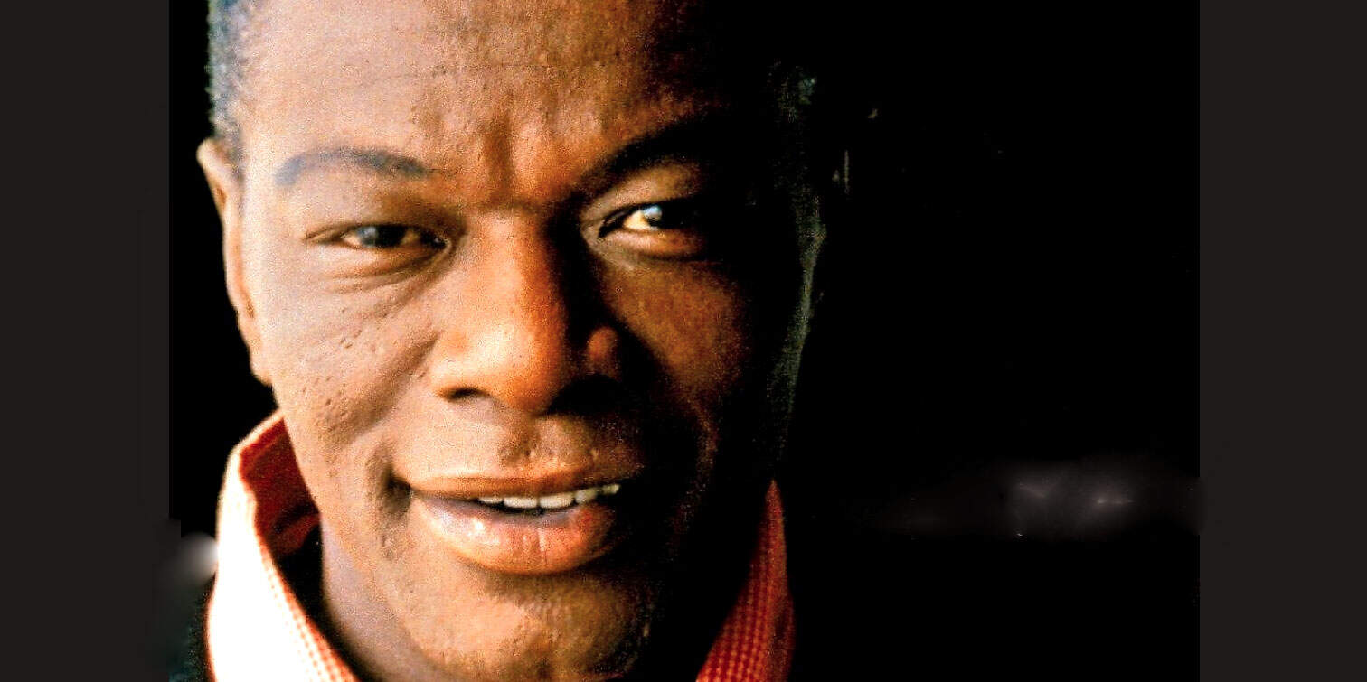 Close-up of a smiling African American man with short hair, wearing a red shirt, captured in a photograph emphasizing his facial features and expression.