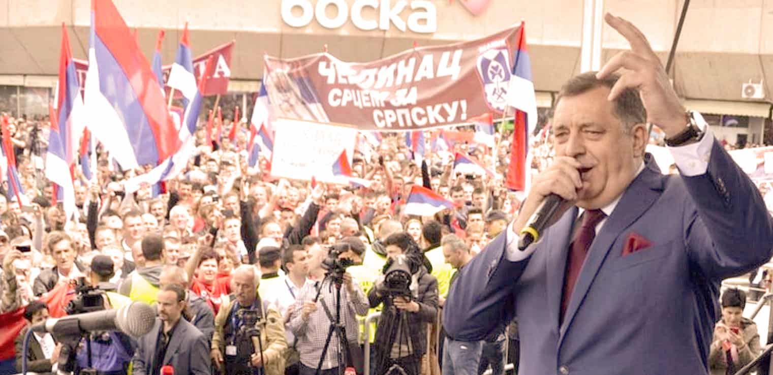 Serbian political leader speaking at a rally with protest signs and flags, addressing supporters during a demonstration promoting Serbian unity and sovereignty.