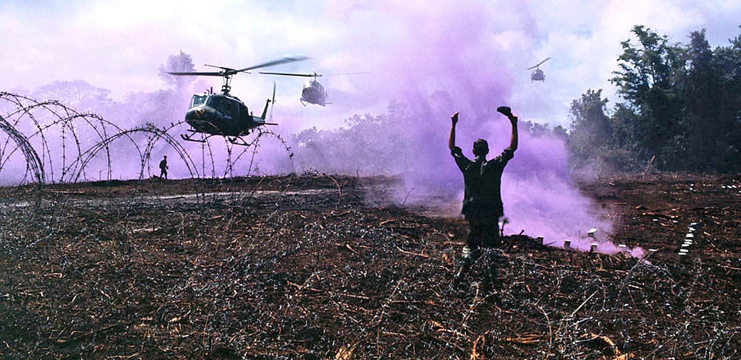 Helicopters flying over a smoky battlefield with a soldier raising his arms in the foreground, capturing a scene of conflict and chaos.