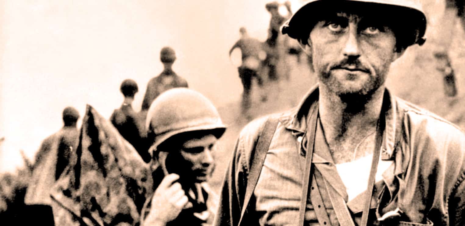 Soldier and war zone photo from World War II history archive, depicting soldiers in combat attire, with a soldier in the foreground and others in the background; historical news and war documentaries.