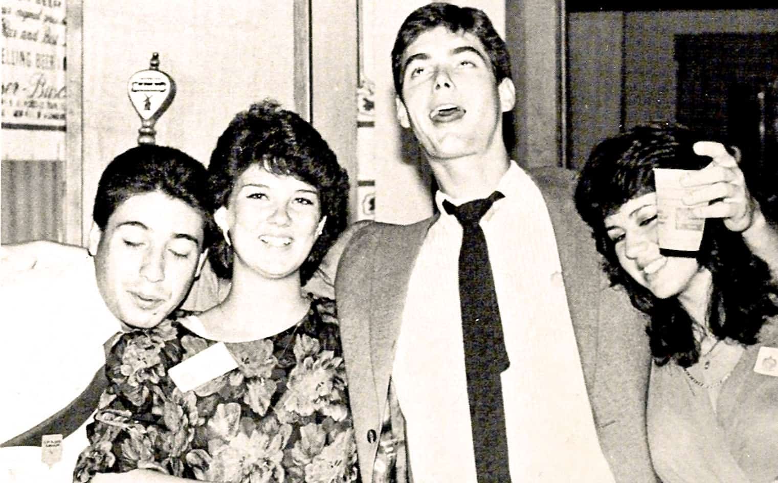 Old black and white photo of four young adults at a social event, smiling and enjoying themselves, representing the lively music, news, and history archive by Past Daily.