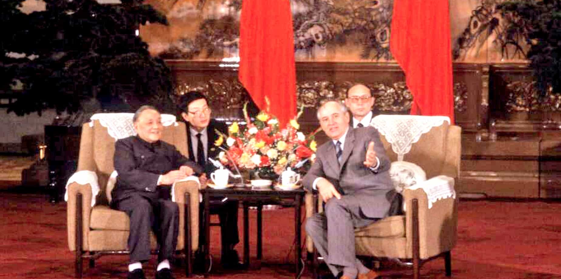 Historic political leaders sitting together in a formal setting, surrounded by traditional Chinese decor and red drapes, representing a significant event in Chinese history.