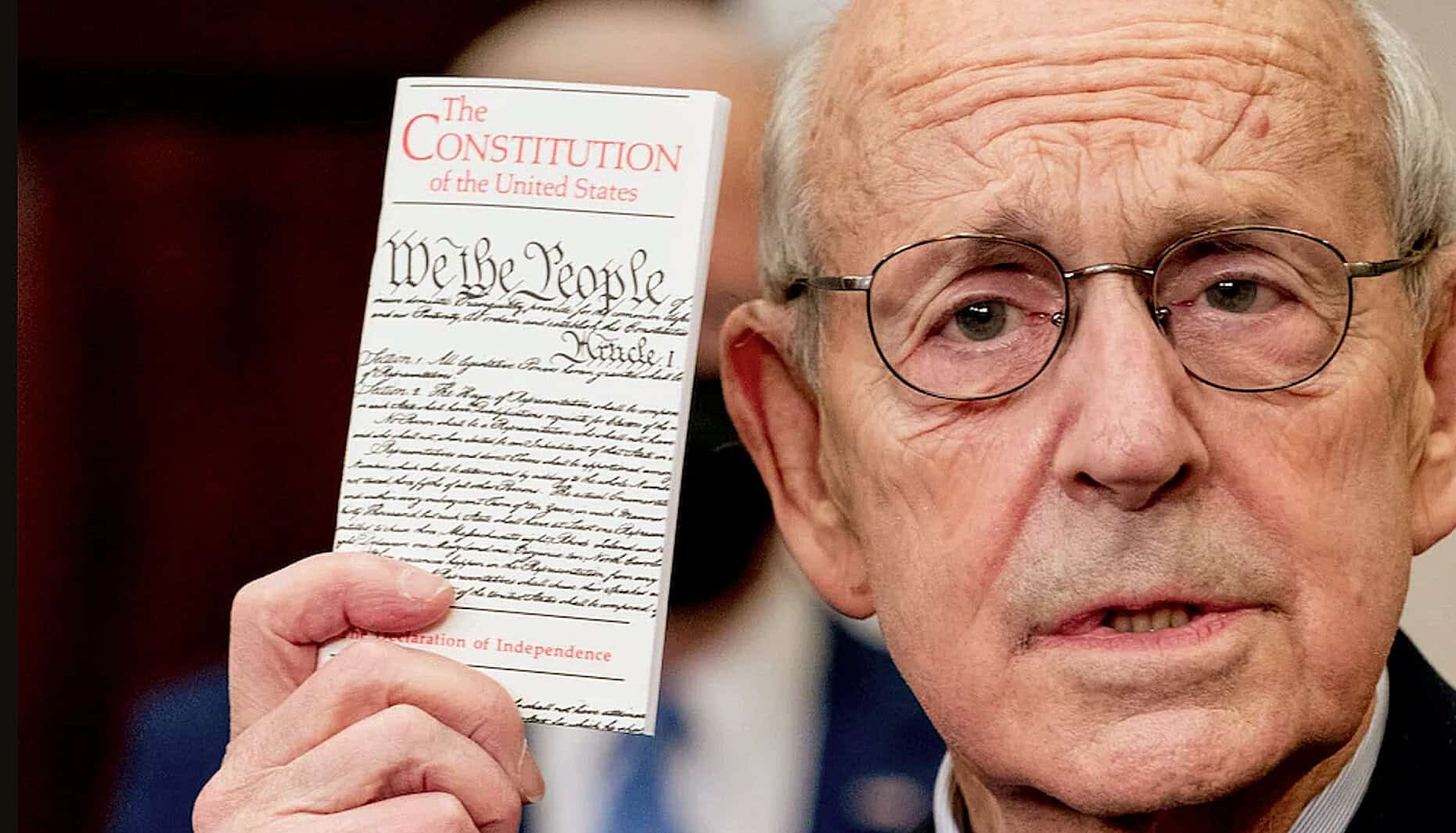 A close-up of U.S. President Joe Biden holding a copy of the U.S. Constitution during a formal event, highlighting historical and political significance related to American independence and government.
