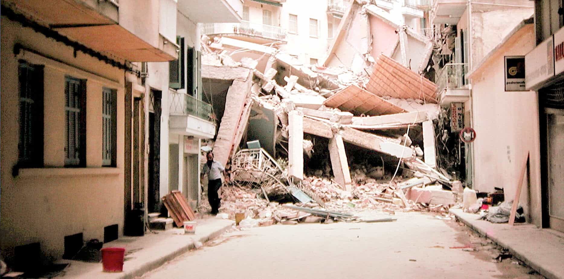 Collapsed building debris in an urban street after an earthquake, with rescue efforts visible. Focuses on disaster, earthquake aftermath, urban destruction, and emergency response, emphasizing historic seismic events.