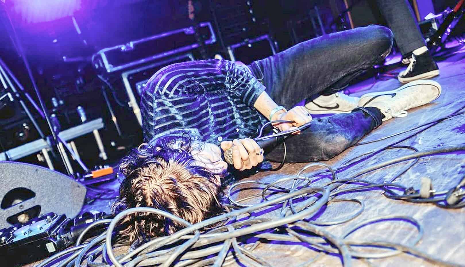 Vocalist performing live on stage with cables and music equipment, showcasing the energetic atmosphere of a concert or music event.