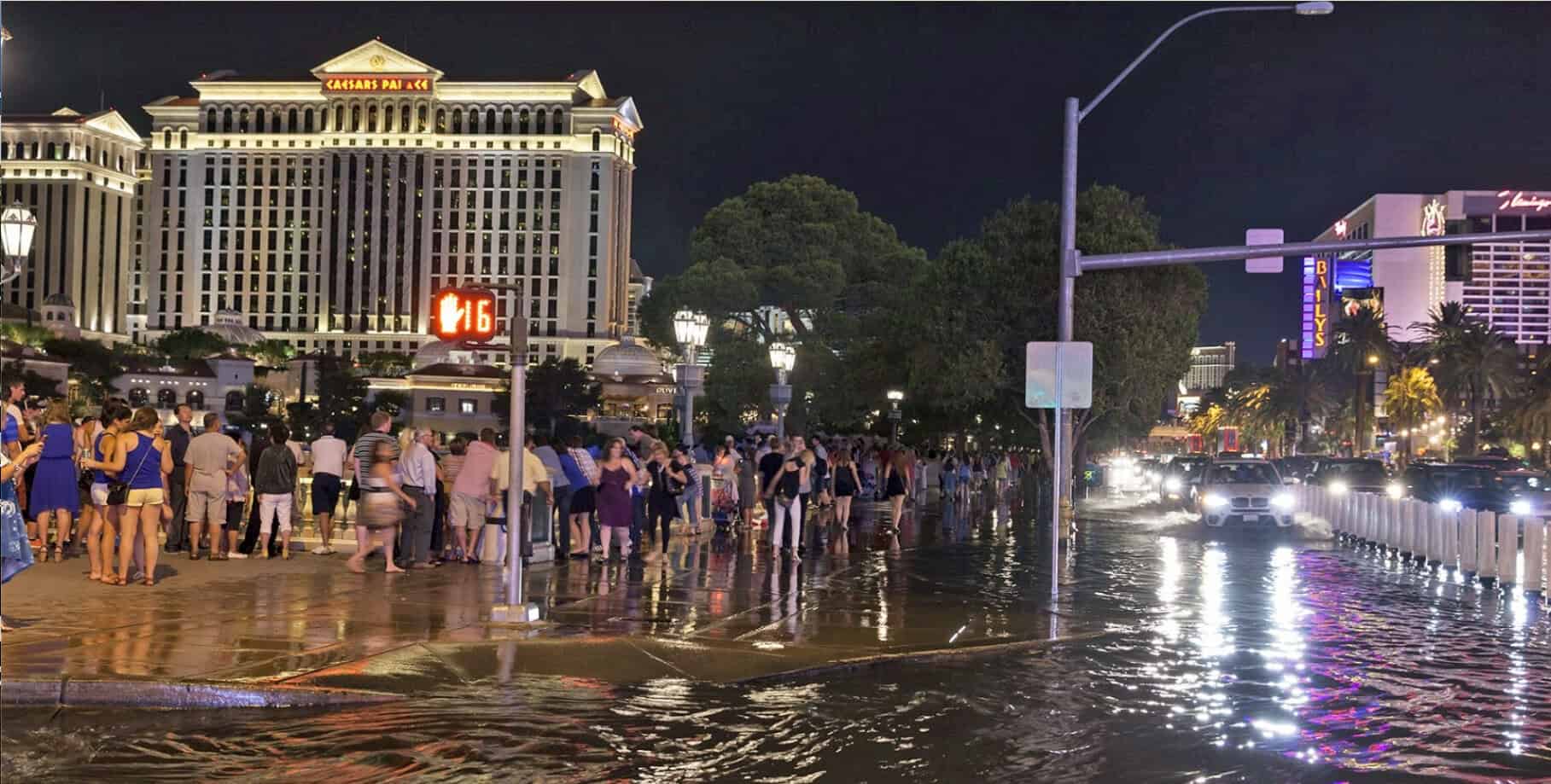 Flooded street at night with pedestrians, bright city lights, and iconic casinos in the background, capturing Las Vegas nightlife and urban atmosphere.