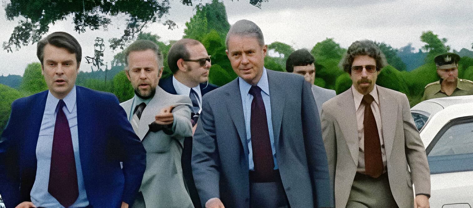 A vintage scene from the TV series "Yes Minister," featuring government officials in suits walking outside, representing classic political satire and British television history.