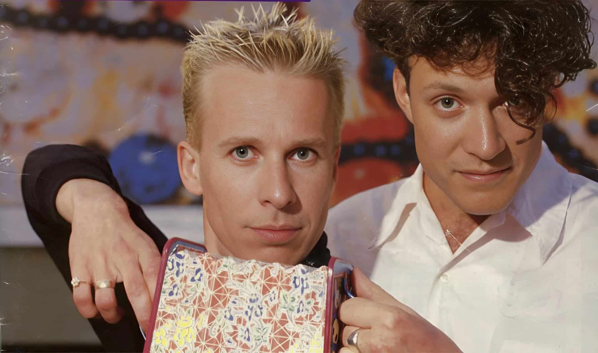 Two young men with vibrant personalities, one with short blond hair and the other with curly dark hair, pose closely together. They represent themes of friendship, music, and pop culture, emphasizing the entertainment value of the past daily sound archive.