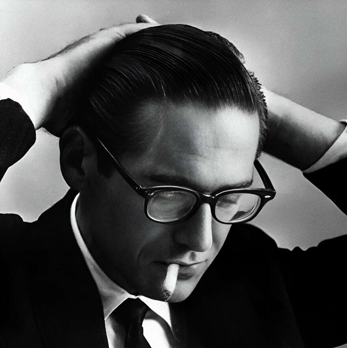 Vintage black and white photograph of a man with slicked-back hair, glasses, smoking a cigarette, representing historical news, music, and audio archive themes from Past Daily.