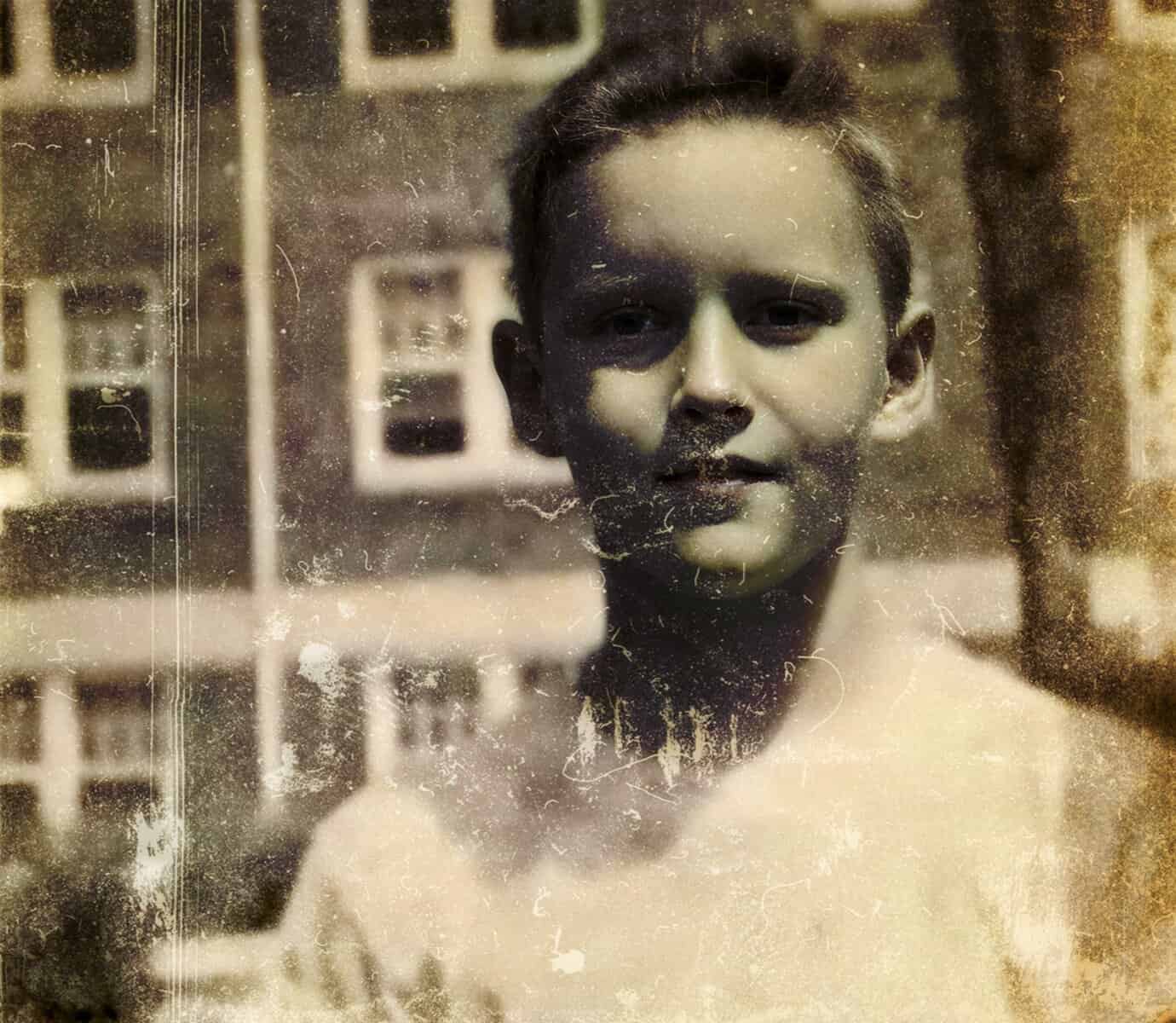 Historic black and white photograph of a young boy with a background of vintage buildings, capturing nostalgic moments from early 20th-century life, emphasizing history, childhood, and archival news imagery.