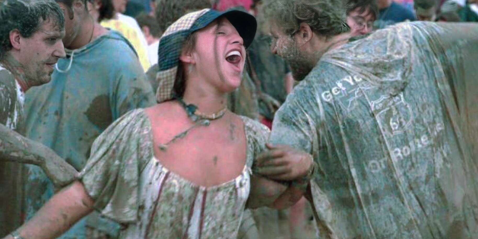 Colorful crowd at a lively music festival with people covered in mud, smiling and enjoying the moment during a festival celebration.