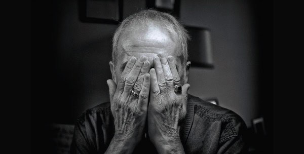 Old man covering his face with hands, expressing emotion or distress, in a black and white image.