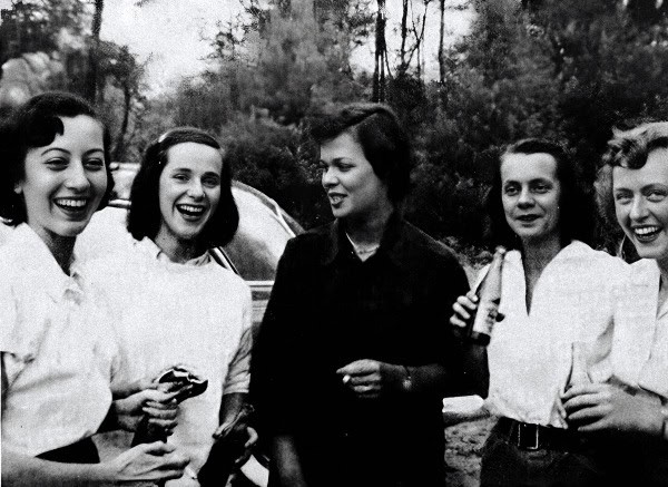 Women soldiers smiling and chatting outdoors during World War II, capturing a historic moment of female participation in wartime efforts, emblematic of resilience and camaraderie.