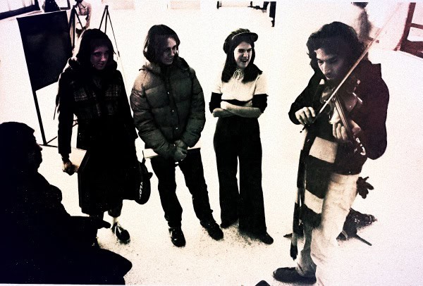A black and white image of a street musician playing the violin for a small audience, capturing a candid moment of street-performing music, popular in urban entertainment scenes.