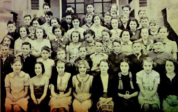 Students gathered outside school building, vintage photo from early 20th century, historical classroom scene, old schoolchildren, archival educational photo, Past Daily history archive, nostalgic learning environment.