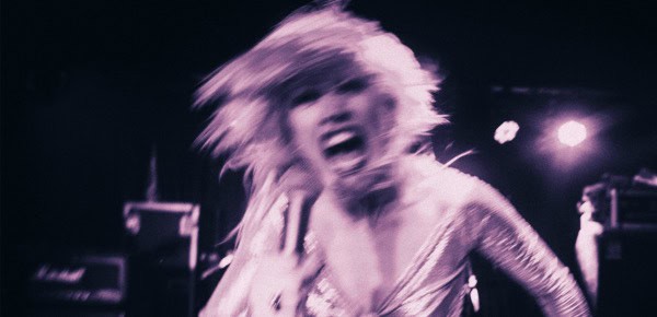 Vintage black and white photo of a female rock singer performing energetically on stage, capturing the spirit of music history and live performance.