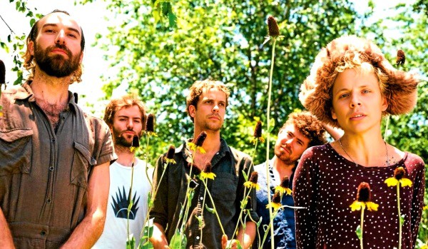 Natural outdoor scene with a young female voice singer and a band in the background, vibrant greenery, music performance, concert, and music band imagery.