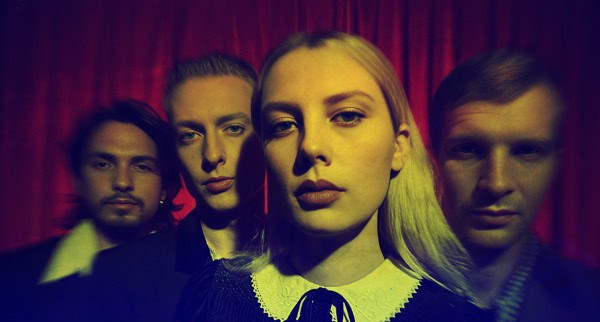 Vintage band members portrait with dramatic red curtain background, reflecting music history and entertainment archives.