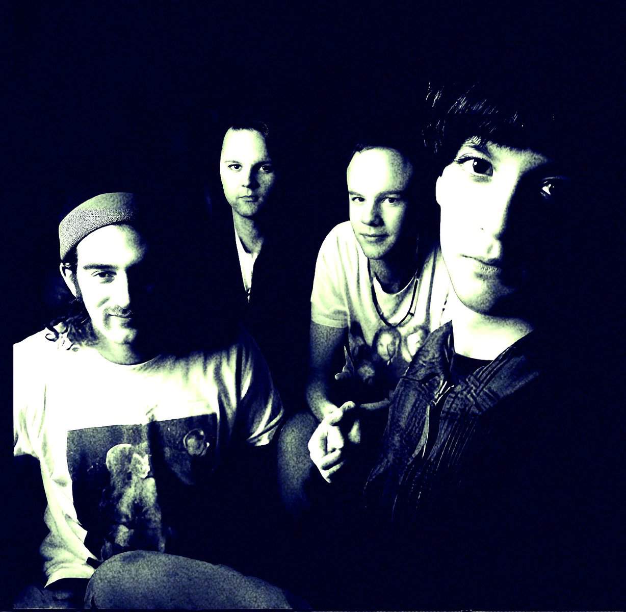 Limited edition band photo of four young men in a dimly lit setting, showcasing their musical style. Perfect for music history and nostalgic sound archive content related to 90s rock or indie bands.