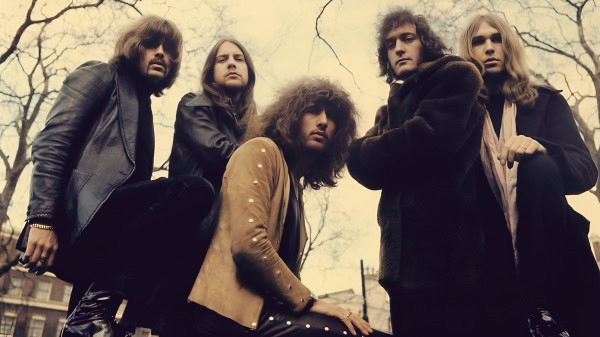 Vintage rock band outdoor photoshoot with overcast sky, emphasizing classic 70s music style, edgy fashion, and atmospheric setting.