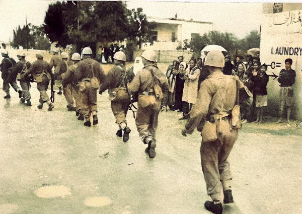 Policemen patrolling a street during a historical event, with onlookers watching nearby, reflecting a moment of social or political significance captured in a vintage photo.