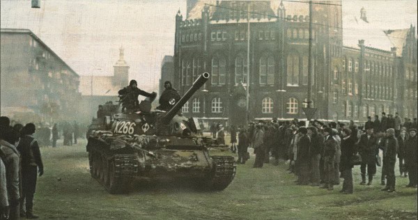 Tank surrounded by people in an urban setting during a historical event.