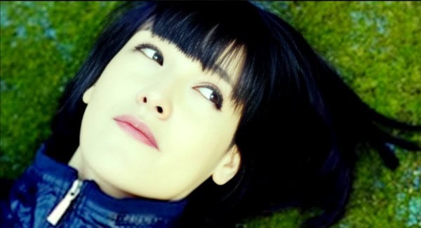 Vibrant woman lying on green grass outdoors, enjoying music and relaxation, representing sound archive and historical audio content from Past Daily.