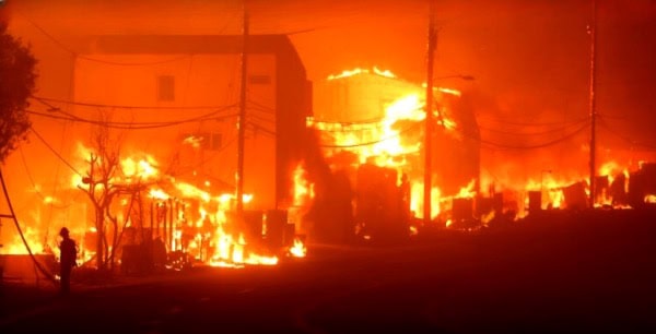 Severe house fire at night with flames engulfing multiple buildings, emergency response in progress, emphasizing disaster, fire safety, and emergency recovery.