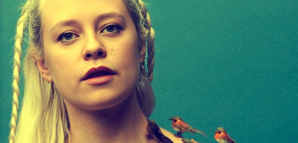 A-young woman with braided blonde hair and blue eyes against a green background, symbolizing nostalgia and history in audio archives.
