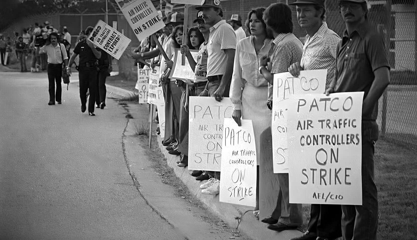 Protesters holding signs demanding air traffic controllers strike, illustrating labor disputes and activism; black-and-white photo showcasing social movement and workers' rights.