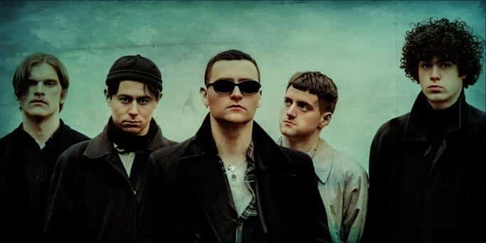 A grayscale photo of a rock band with five members, emphasizing their edgy style and serious expressions, representing music history and cultural influence.