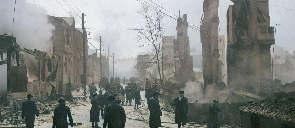 Ruins of a destroyed building with smoke and debris, historical war damage scene, people walking through the rubble, vintage black-and-white photo, reflecting past conflicts and disaster aftermath.