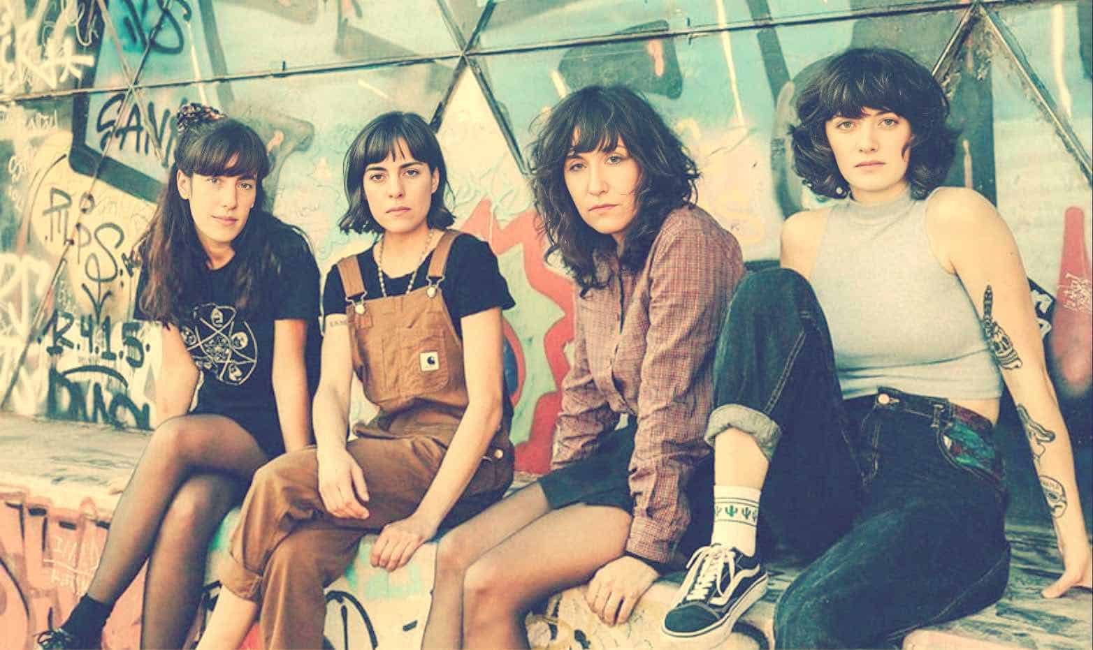 Vintage indie girl band posing against colorful graffiti wall, showcasing alternative fashion and music culture, perfect for exploring 90s rock, female musicians, and urban art scenes.