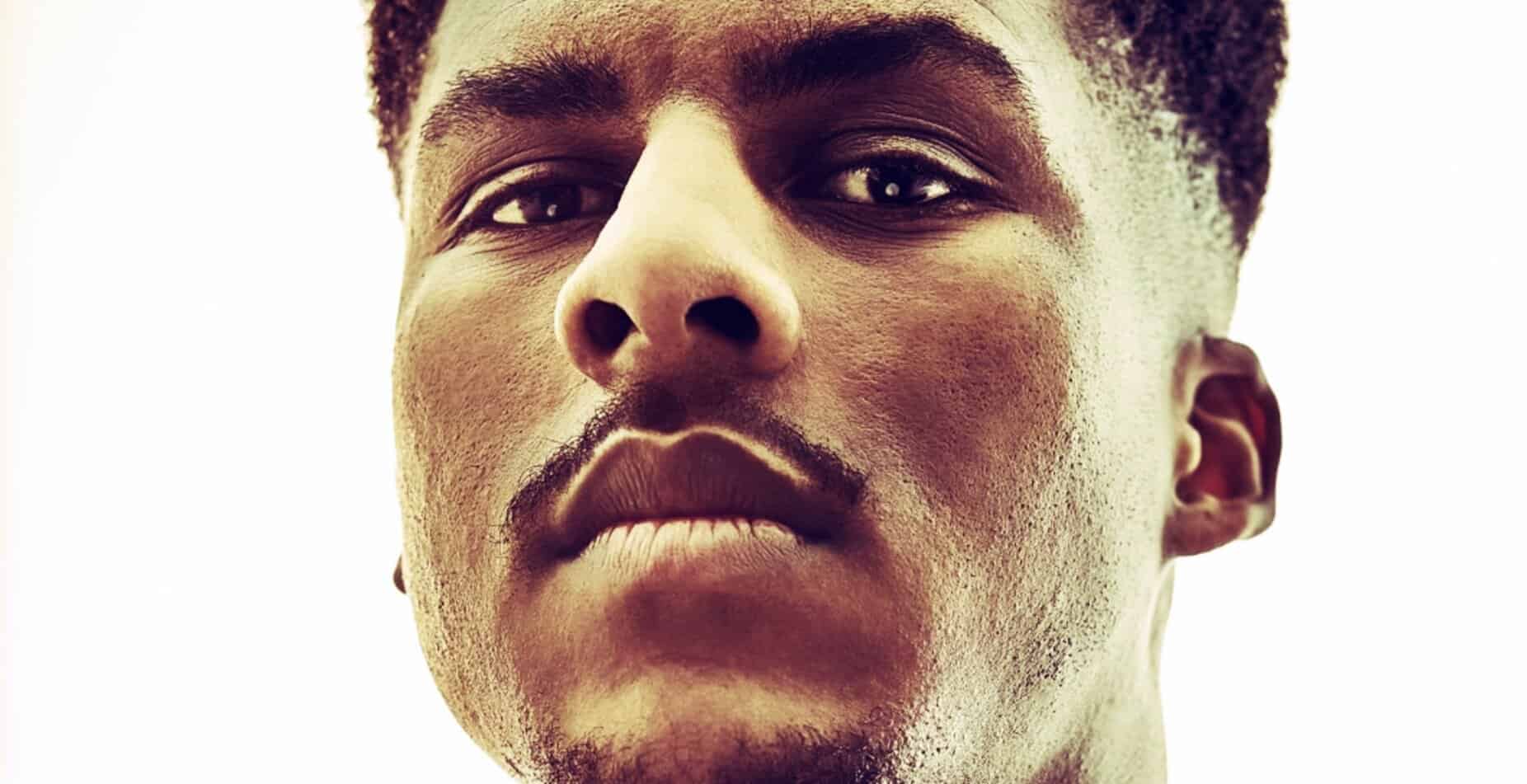 Close-up portrait of a young African American man with confident expression, highlighting detailed facial features, smooth skin, and natural hair, representing themes of identity and culture.