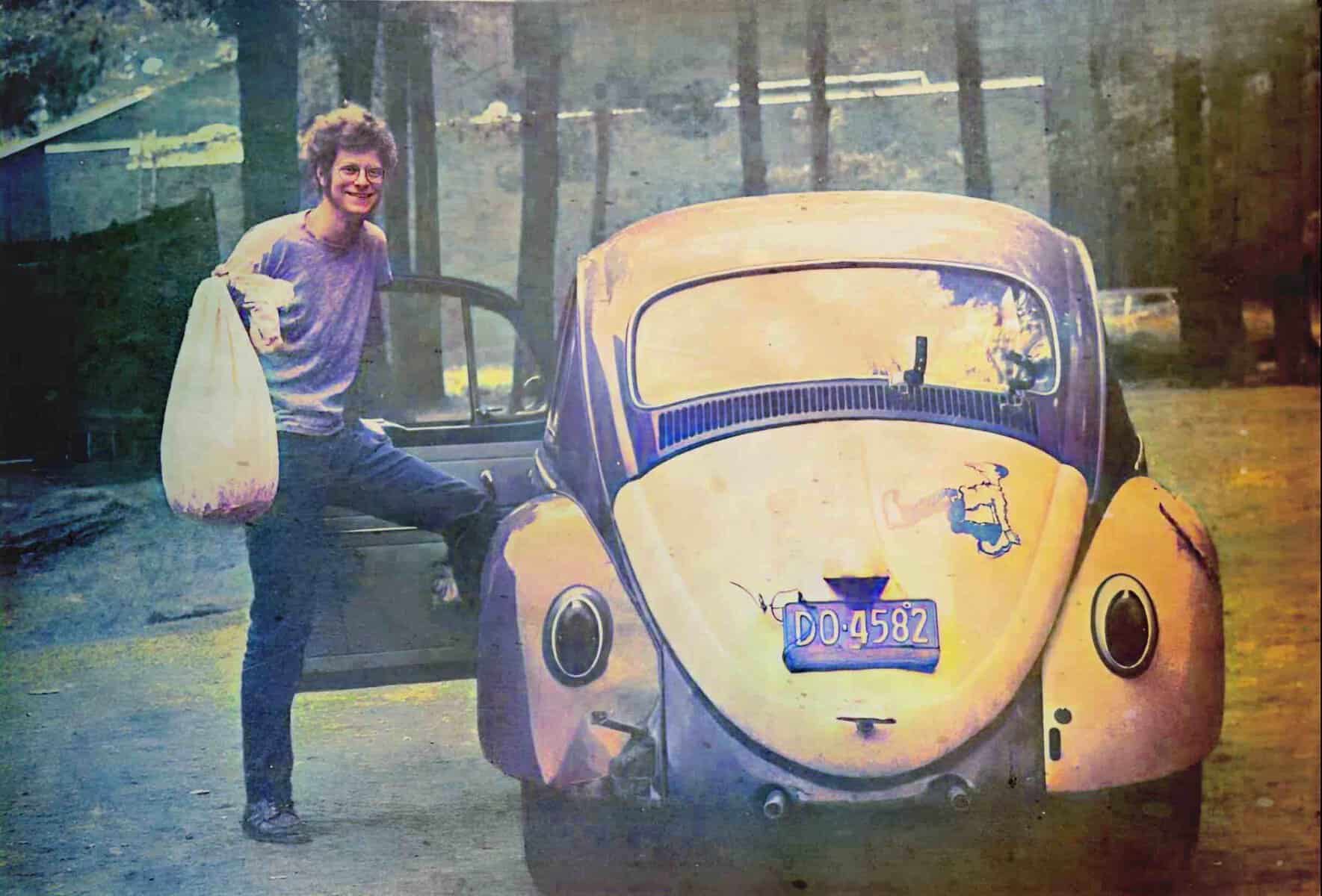 Vintage yellow microcar parked in a park with a woman holding a shopping bag and sitting on the open door, capturing the essence of classic transportation.